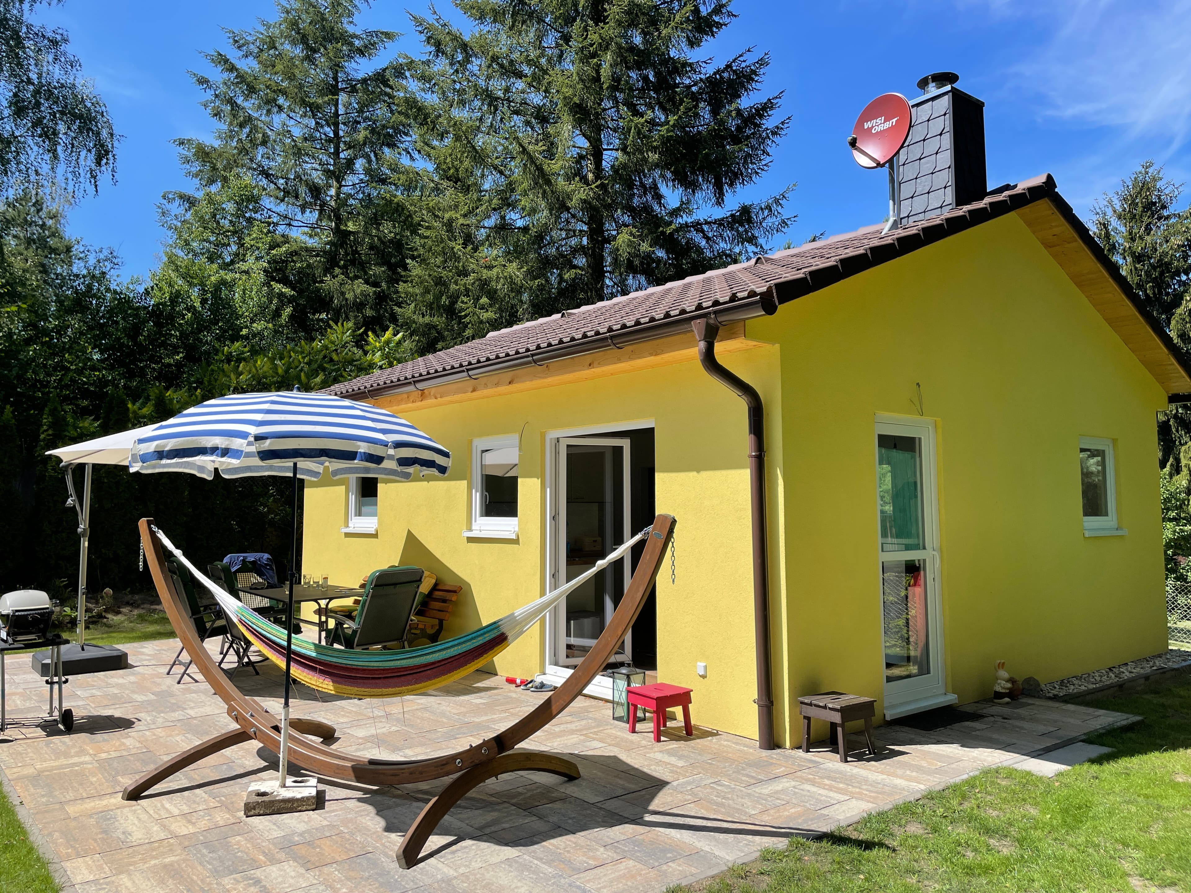 Gelbes Ferienhaus mit Terrasse, Hängematte und Sonnenschirm im Garten