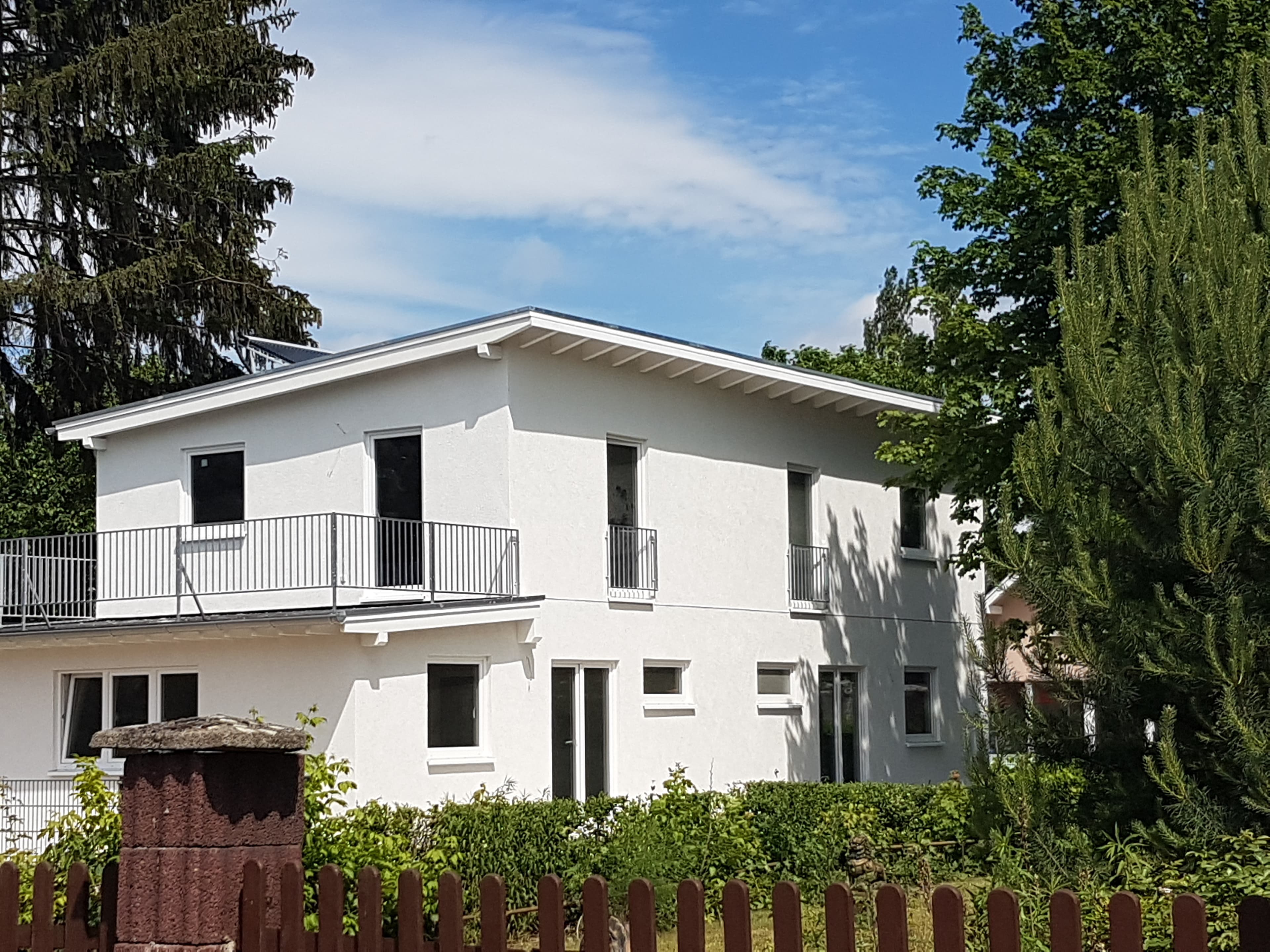 Weißes Doppelhaus mit Balkon hinter einem Holzzaun