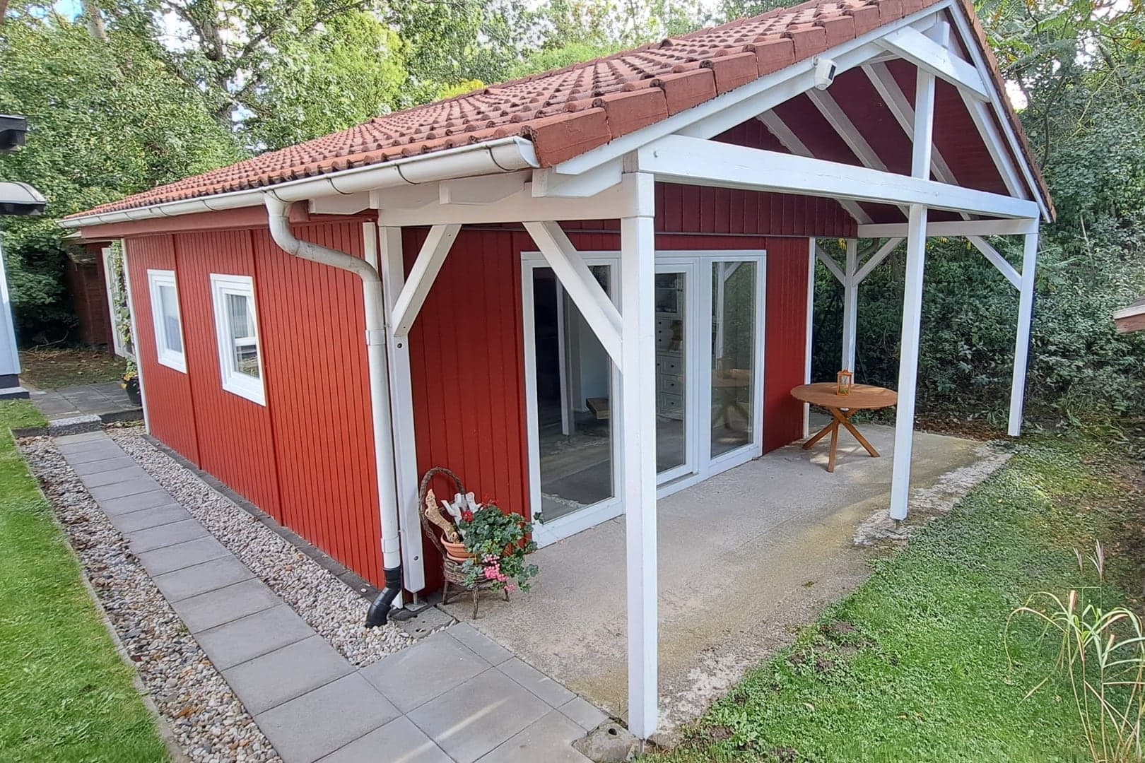 Musterhaus Bodensee 01 im Park: rotes Ferienhaus mit weißer Pergola