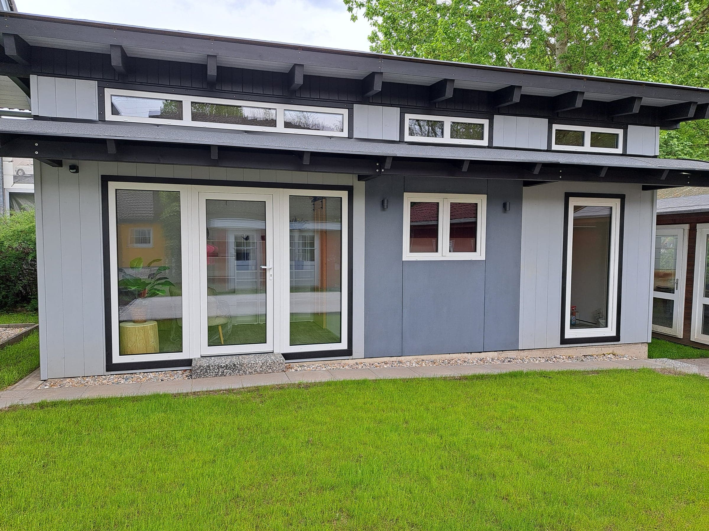 Musterhaus Elipsa 01 im Park: graues Haus mit flachem Dach und Rasenfläche