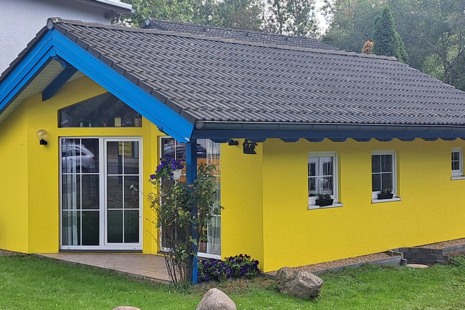 Musterhaus Kerstin F1 im Park: gelber Bungalow mit blauem Giebel und Terrasse