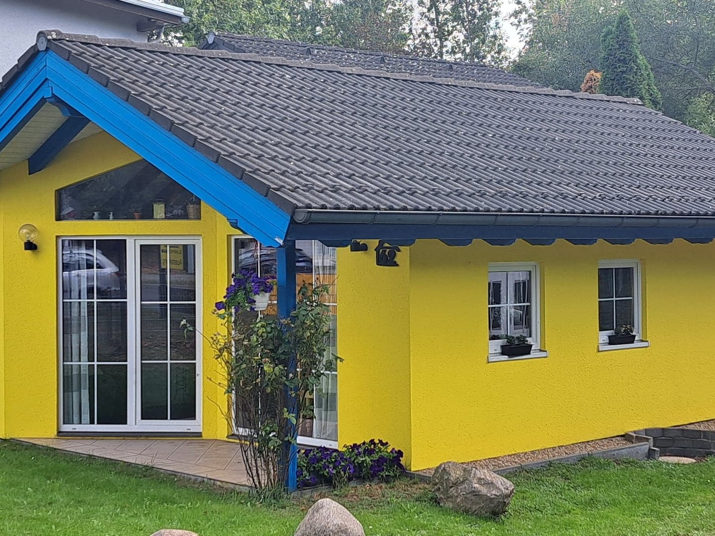 Musterhaus Kerstin F1 im Park: gelber Bungalow mit blauem Giebel und Terrasse