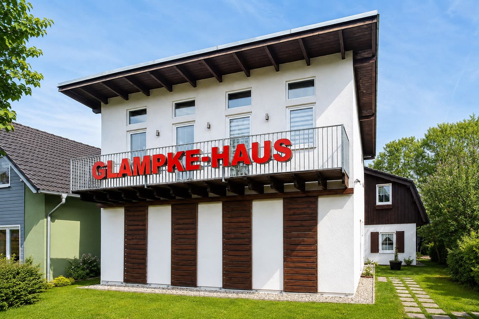 Das Betriebsgebäude der Glampke-Haus GmbH mit dem roten Schriftzug an der Fassade, davor Rasen und ein Plattenweg