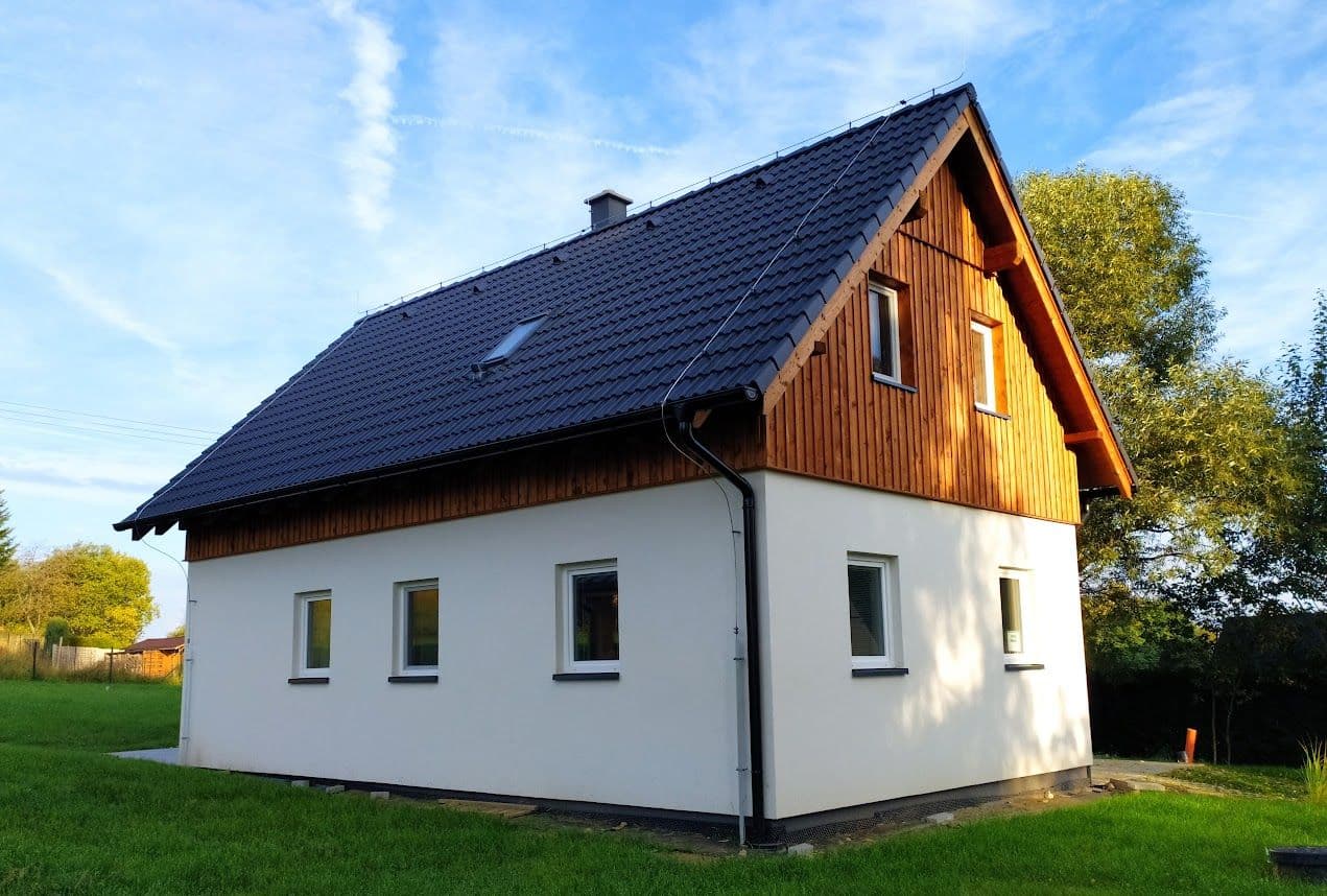 Weißes Haus mit Holzgiebel und dunklem Dach vor weitem Rasen